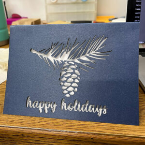 Blue, laser-cut card "happy holidays, pine cone motif