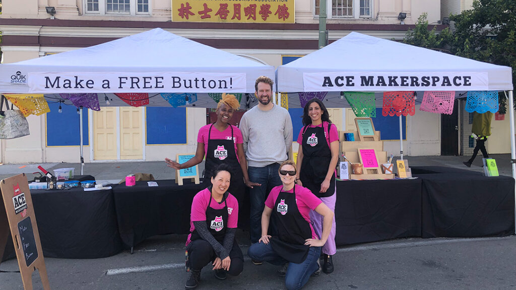 5 people in pink shirts, black aprons, in front of two booths.