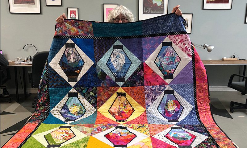 Person holds up colorful quilt.