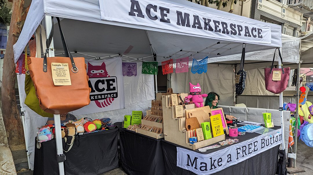 Person at Ace Makerspace Oakland Pride Booth, with maker projects