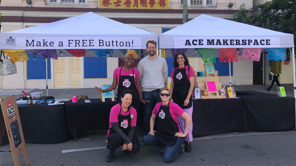 Group posing in "Ace" aprons in front of Ace booth.